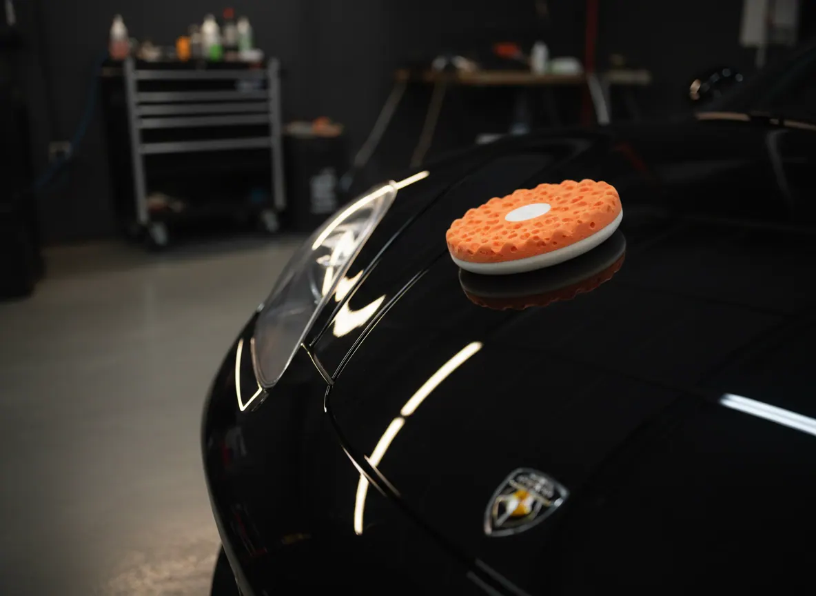 A polisher pad resting on the glossy, swirl-free black hood of a car after paint correction